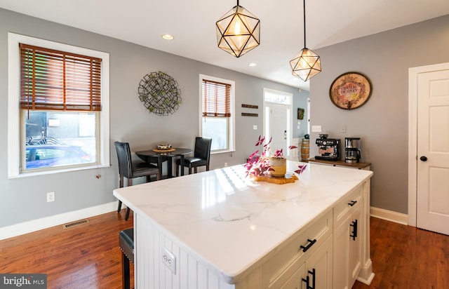 kitchen with light stone counters, hanging light fixtures, and a healthy amount of sunlight