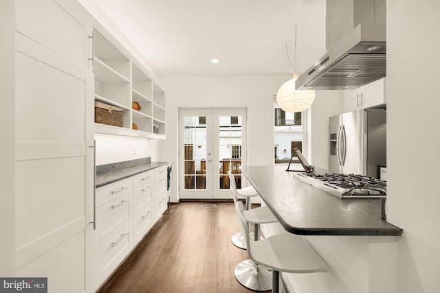 kitchen featuring white cabinets, dark hardwood / wood-style flooring, appliances with stainless steel finishes, wall chimney exhaust hood, and decorative light fixtures