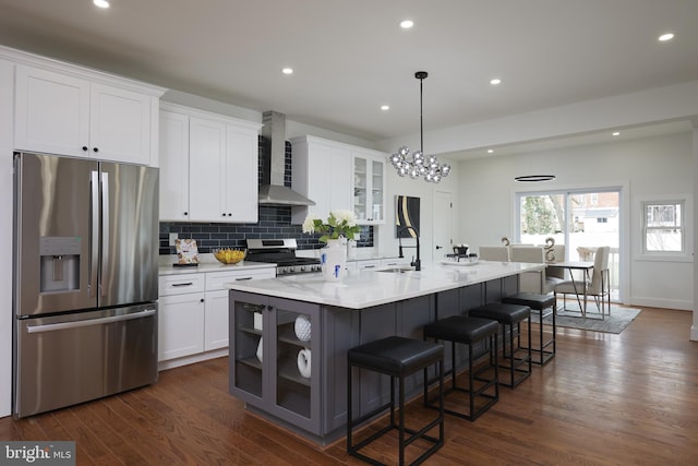 kitchen with a kitchen island with sink, white cabinets, wall chimney range hood, appliances with stainless steel finishes, and a kitchen bar