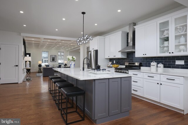 kitchen featuring white cabinetry, a large island, wall chimney exhaust hood, pendant lighting, and appliances with stainless steel finishes