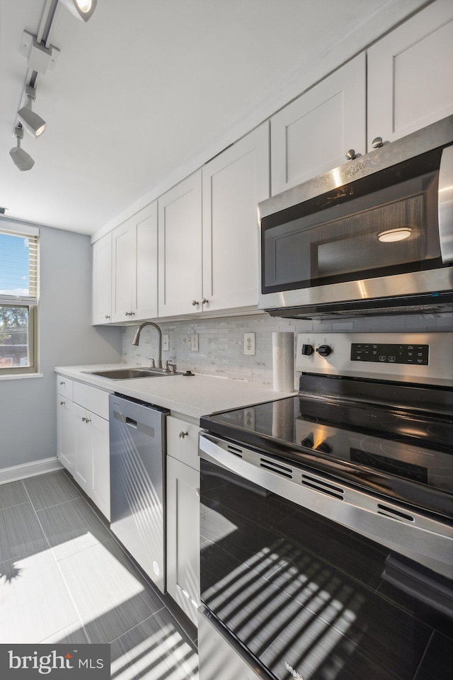 kitchen featuring decorative backsplash, white cabinets, light tile patterned floors, appliances with stainless steel finishes, and sink