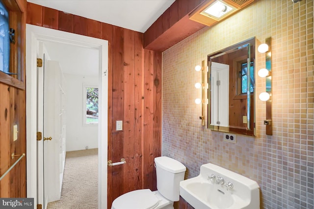 bathroom with tile walls, toilet, wooden walls, and sink