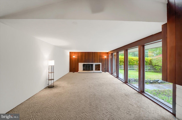 unfurnished living room featuring carpet flooring, wooden walls, and lofted ceiling