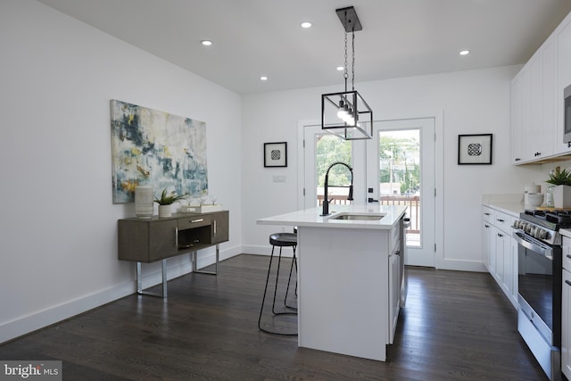 kitchen with stainless steel range with gas cooktop, sink, white cabinets, a center island with sink, and decorative light fixtures