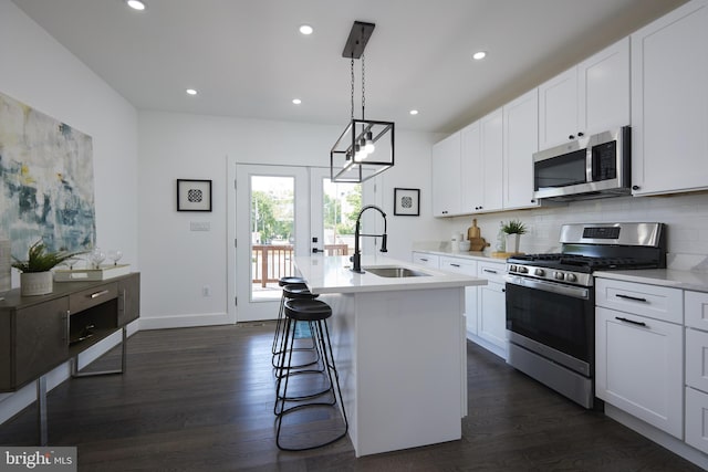 kitchen featuring white cabinets, stainless steel appliances, decorative light fixtures, a kitchen island with sink, and sink