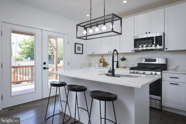 kitchen featuring white cabinets, hanging light fixtures, a kitchen island with sink, stainless steel appliances, and dark hardwood / wood-style flooring