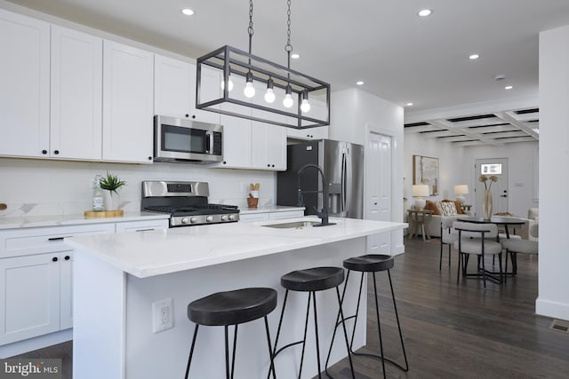 kitchen featuring appliances with stainless steel finishes, a kitchen island with sink, dark hardwood / wood-style flooring, and white cabinetry