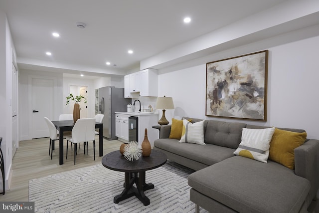 living room with wine cooler, light wood-type flooring, and sink