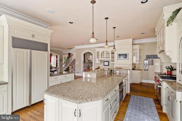 kitchen featuring a kitchen island, premium appliances, crown molding, light hardwood / wood-style flooring, and decorative light fixtures