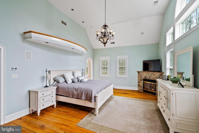 bedroom with a fireplace, light hardwood / wood-style flooring, and high vaulted ceiling