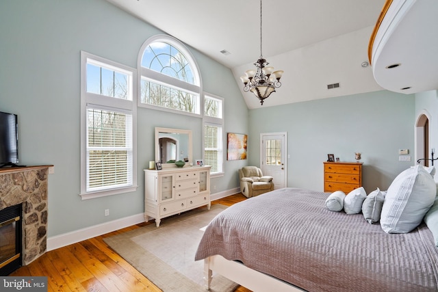 bedroom featuring a stone fireplace, hardwood / wood-style flooring, a notable chandelier, and high vaulted ceiling