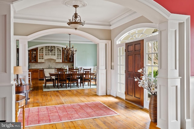 foyer entrance featuring wood-type flooring, ornamental molding, sink, and a notable chandelier