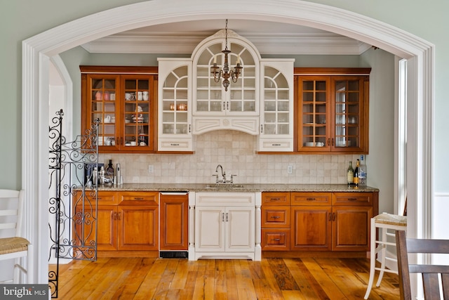 bar with light wood-type flooring, light stone counters, hanging light fixtures, and tasteful backsplash