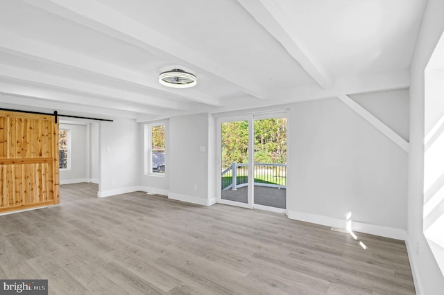 unfurnished living room featuring beamed ceiling, a barn door, and light hardwood / wood-style flooring