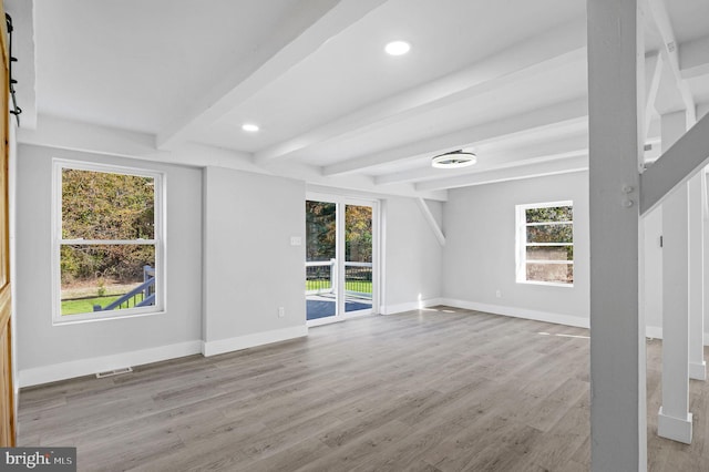 unfurnished living room featuring a barn door, light hardwood / wood-style flooring, beamed ceiling, and a healthy amount of sunlight