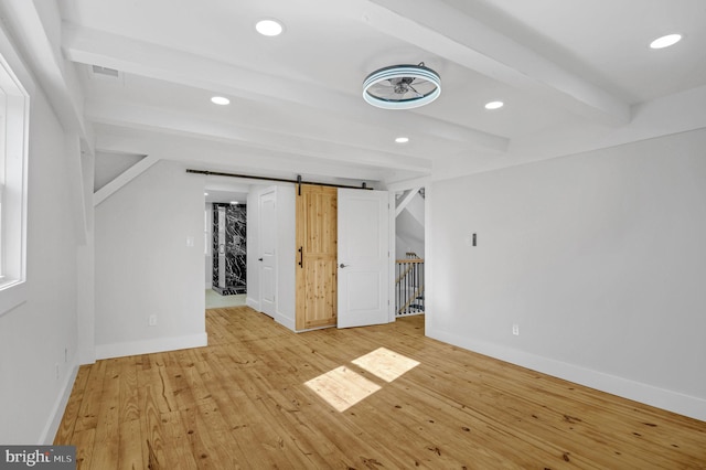 unfurnished room featuring a barn door, beamed ceiling, and light hardwood / wood-style floors