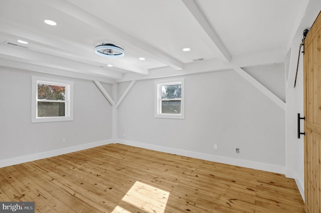 bonus room with beam ceiling, a barn door, a healthy amount of sunlight, and hardwood / wood-style flooring