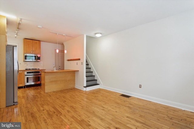 kitchen with light hardwood / wood-style floors, kitchen peninsula, appliances with stainless steel finishes, rail lighting, and decorative backsplash