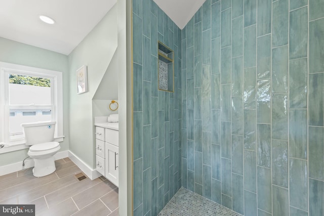 bathroom featuring a tile shower, vanity, and toilet