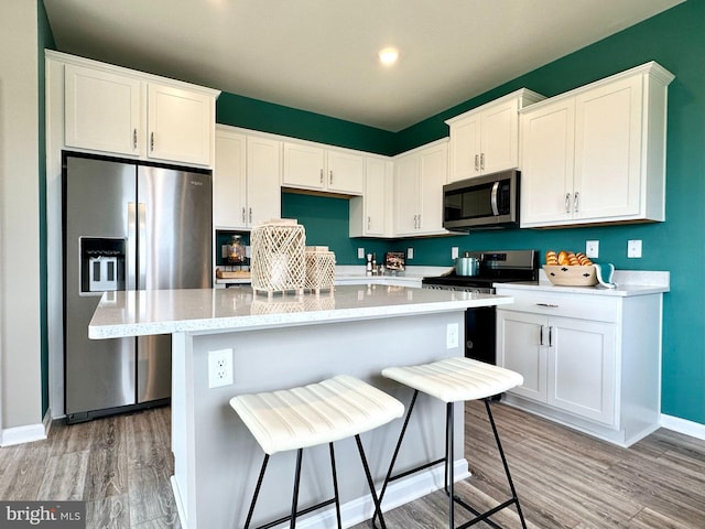 kitchen with a breakfast bar area, white cabinetry, a kitchen island, light hardwood / wood-style flooring, and stainless steel appliances