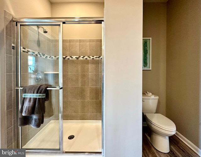 bathroom featuring hardwood / wood-style flooring, a shower with shower door, and toilet