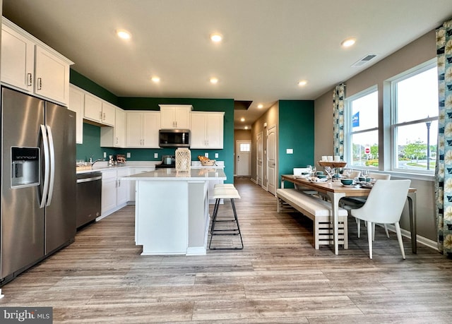 kitchen with a kitchen island, light hardwood / wood-style flooring, white cabinetry, stainless steel appliances, and a kitchen bar