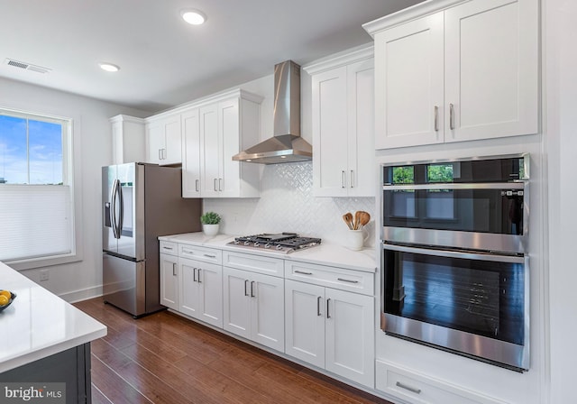 kitchen featuring wall chimney exhaust hood, dark wood-type flooring, stainless steel appliances, and white cabinetry