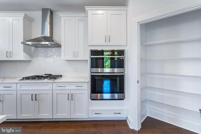 kitchen featuring stainless steel appliances, tasteful backsplash, wall chimney exhaust hood, dark wood-type flooring, and white cabinetry