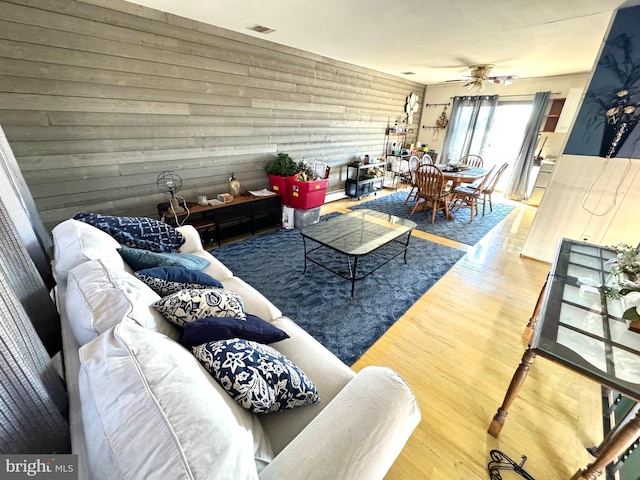 living room with ceiling fan, wood-type flooring, and wooden walls