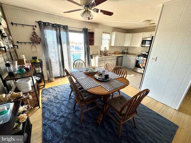 dining space with light hardwood / wood-style floors, ceiling fan, and wooden walls