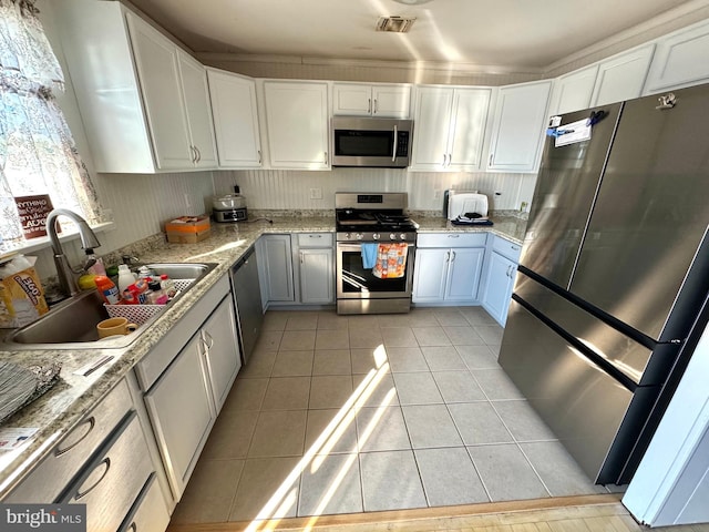 kitchen with appliances with stainless steel finishes, light tile patterned floors, white cabinetry, and sink