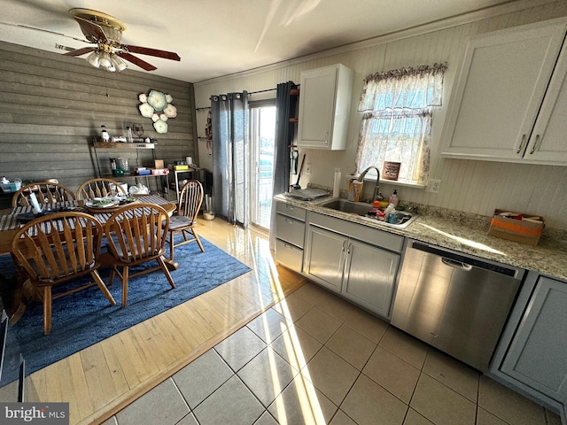 kitchen featuring ceiling fan, sink, dishwasher, light hardwood / wood-style floors, and wood walls