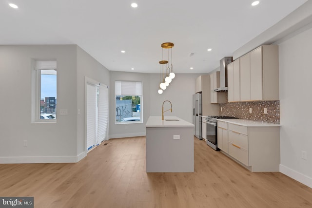 kitchen with a kitchen island with sink, light hardwood / wood-style flooring, pendant lighting, wall chimney exhaust hood, and stainless steel appliances