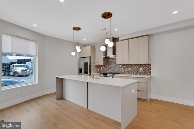 kitchen with a kitchen island with sink, hanging light fixtures, sink, light wood-type flooring, and appliances with stainless steel finishes