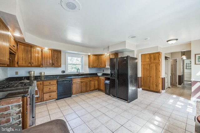 kitchen featuring dark stone counters, black appliances, light tile patterned floors, and sink