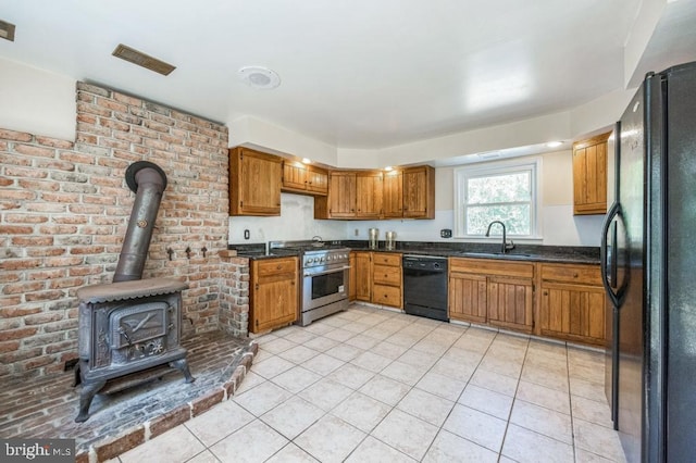 kitchen featuring light tile patterned flooring, sink, a wood stove, black appliances, and brick wall