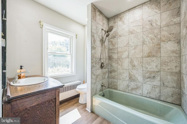 full bathroom with radiator, vanity, tiled shower / bath combo, wood-type flooring, and toilet