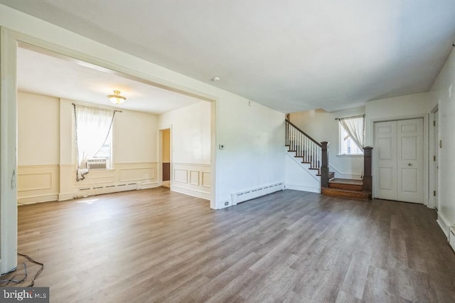 unfurnished living room with hardwood / wood-style flooring, a baseboard heating unit, and a wealth of natural light