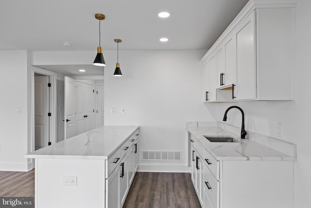 kitchen featuring light stone countertops, dark wood-type flooring, sink, decorative light fixtures, and white cabinetry