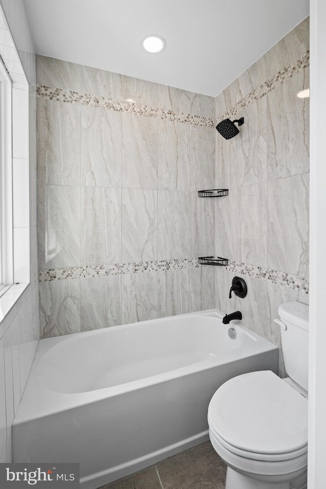 bathroom with washtub / shower combination, tile patterned flooring, toilet, and tile walls