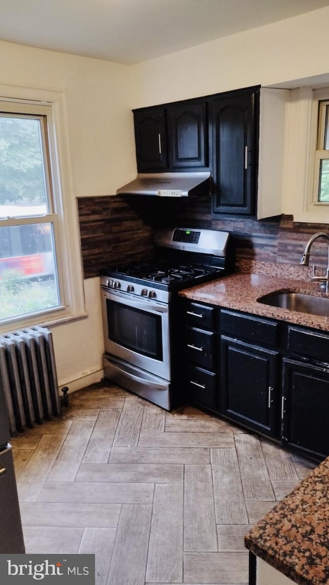 kitchen featuring backsplash, light stone countertops, radiator heating unit, gas stove, and sink