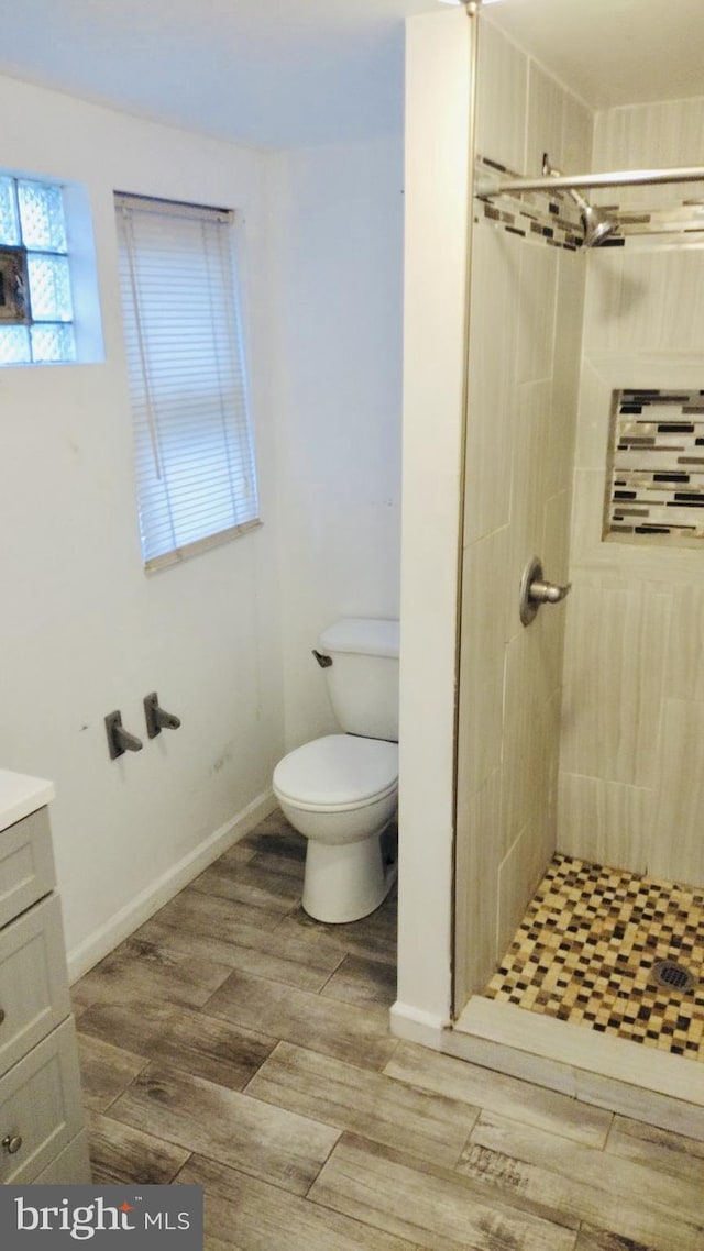 bathroom featuring a tile shower, vanity, toilet, and hardwood / wood-style floors