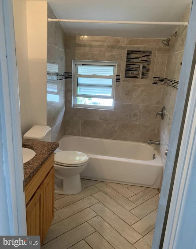 full bathroom featuring tiled shower / bath, vanity, and toilet