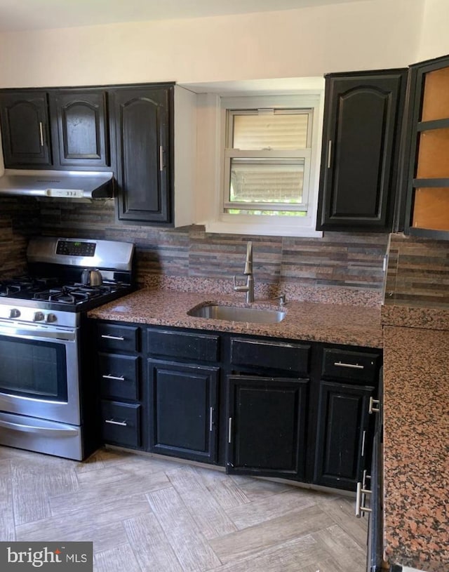 kitchen with dark stone countertops, stainless steel gas stove, sink, and tasteful backsplash