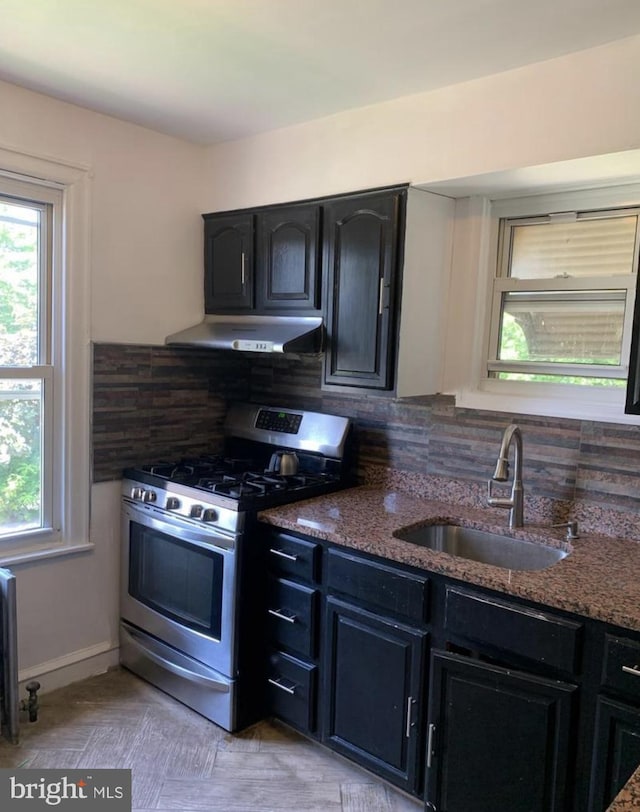 kitchen with decorative backsplash, dark stone countertops, gas range, and sink