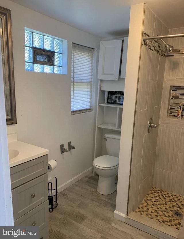 bathroom featuring wood-type flooring, tiled shower, vanity, and toilet