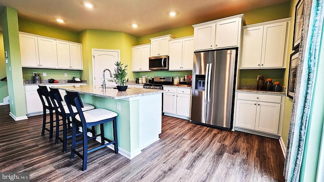 kitchen featuring white cabinets, an island with sink, appliances with stainless steel finishes, light stone countertops, and dark hardwood / wood-style flooring