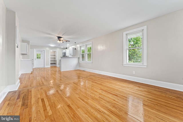 unfurnished living room featuring light hardwood / wood-style flooring, built in shelves, and ceiling fan