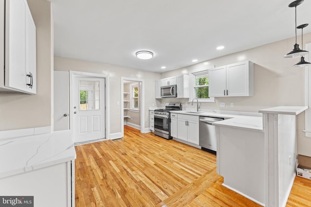 kitchen featuring white cabinetry, decorative light fixtures, stainless steel appliances, and light wood-type flooring