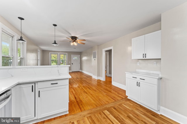 kitchen with kitchen peninsula, ceiling fan, white cabinetry, light hardwood / wood-style flooring, and light stone counters